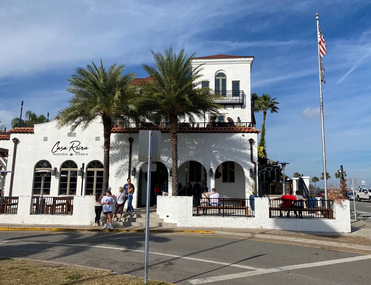 Exterior of Casa Rio with white stucco, red tile roof, palm trees, and outdoor seating.