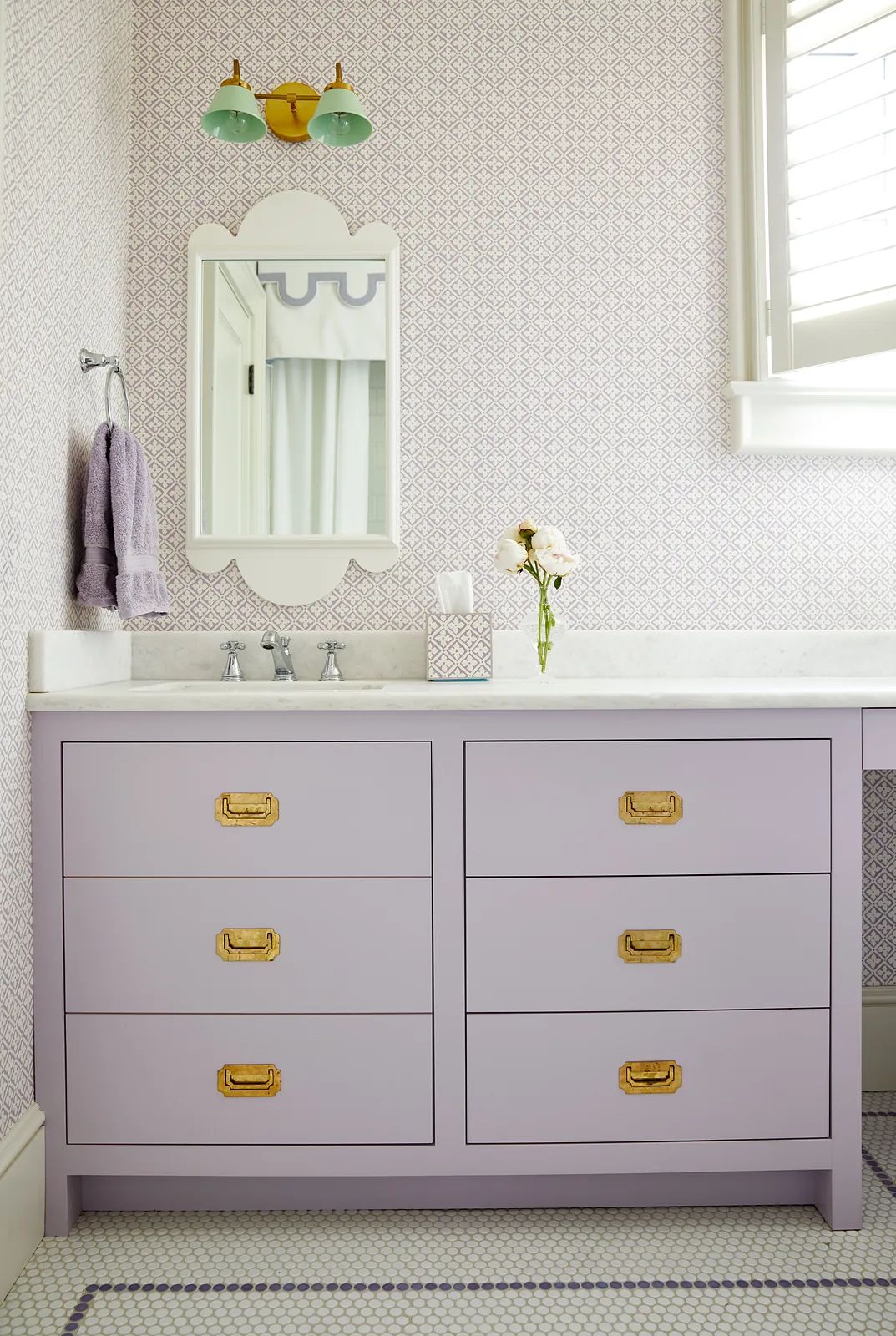 Bathroom with light purple vanity, scalloped mirror, floral decor, patterned wallpaper, and tile flooring.