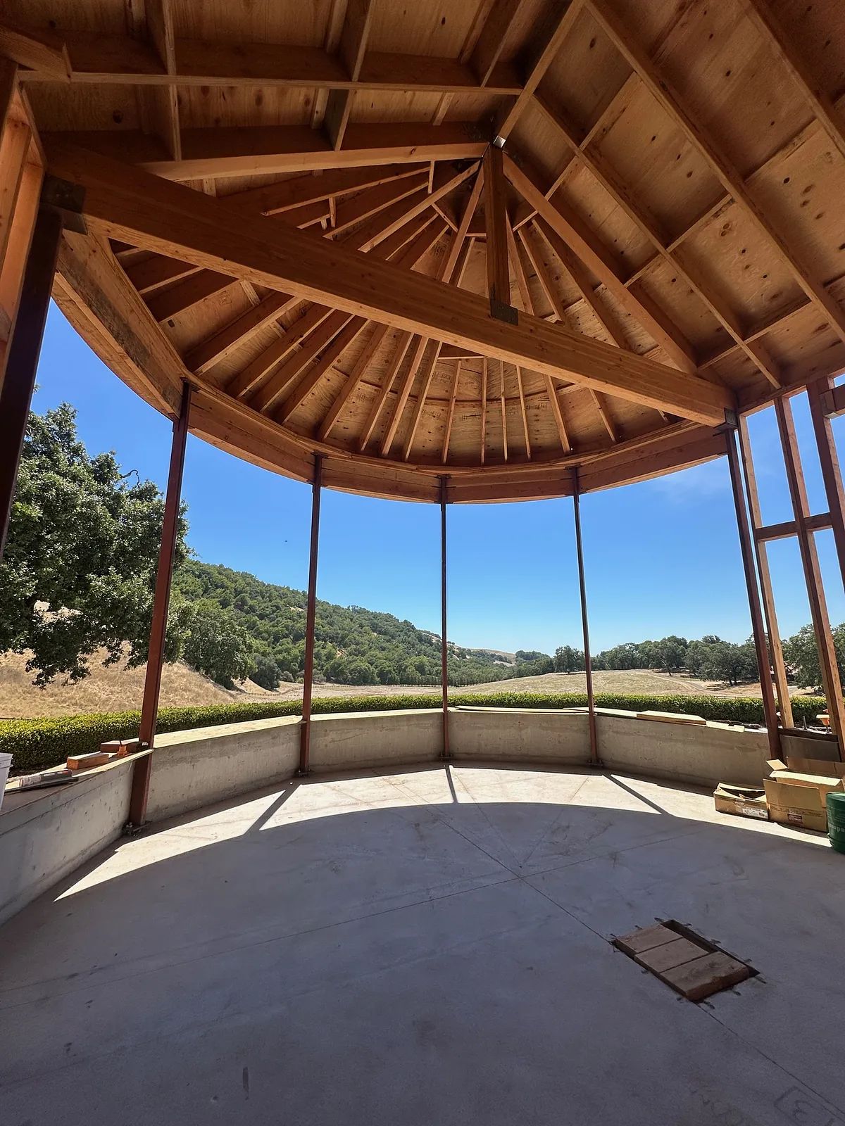 Circular space with wooden beams, large windows, and unfinished walls overlooking a landscape