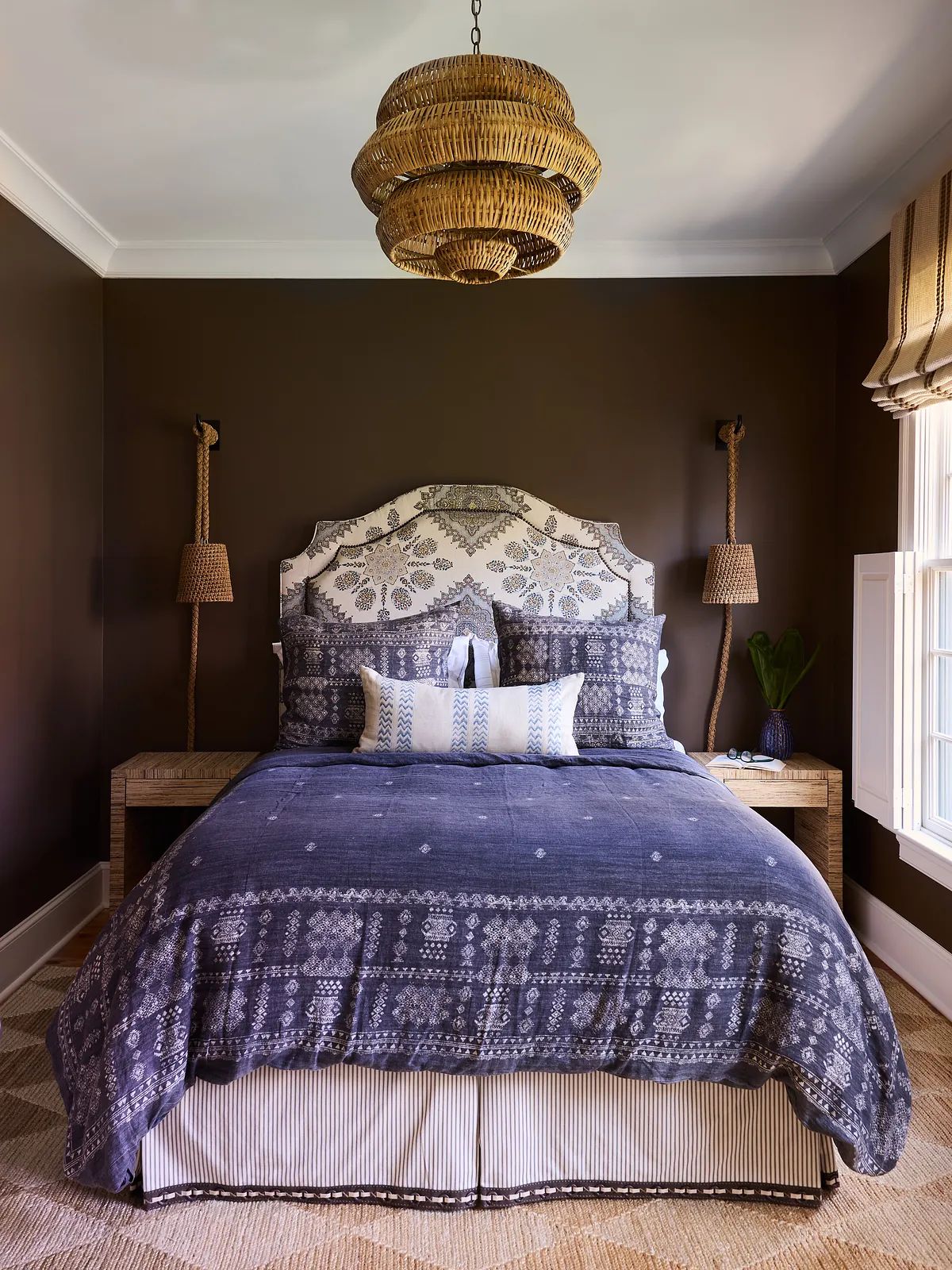 Bedroom with patterned bed, nightstands, sconces, large window, and natural fiber rug.