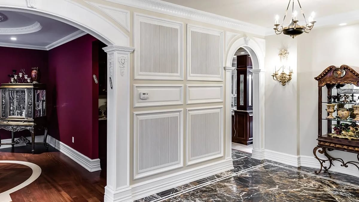 Foyer with white paneling, arches, marble floor, cabinet, chandelier, and wall sconces.