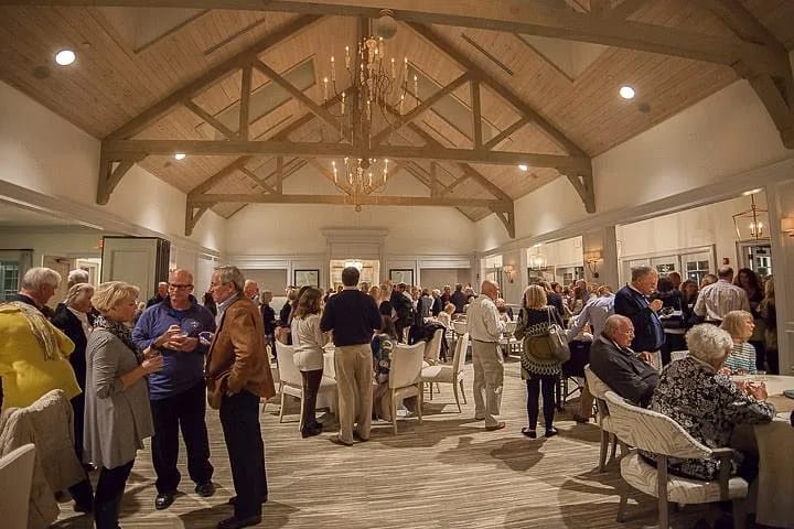 Gathering space with vaulted ceilings, wooden beams, area rug, mirrors, and chandelier with people mingling