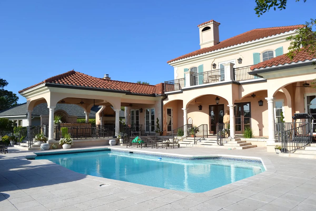 Exterior rear area with swimming pool, tiled patio, columns, and a two-story house with red-tiled roof