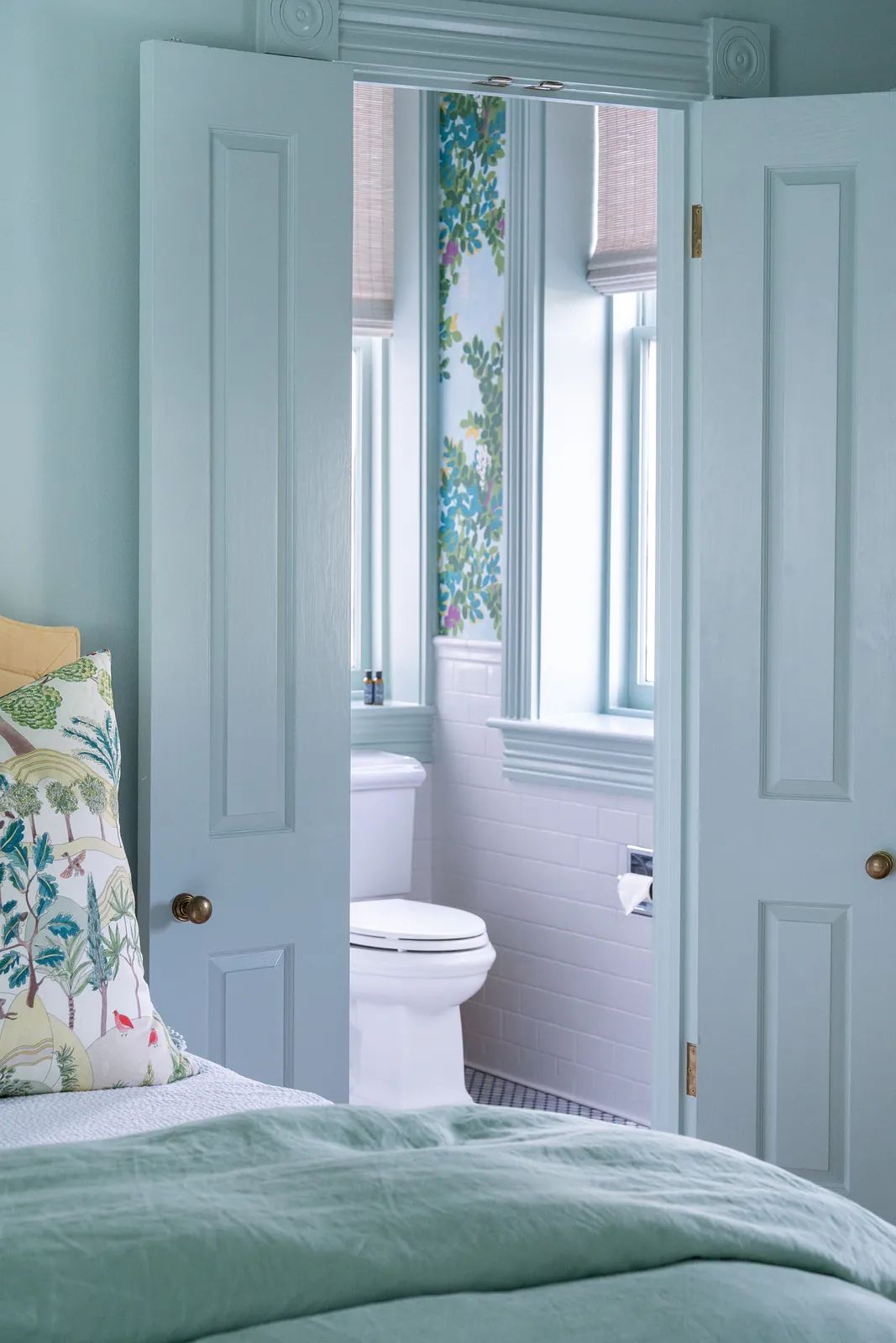 Bathroom with toilet, white tiled wall, light blue paint, and floral window shades.