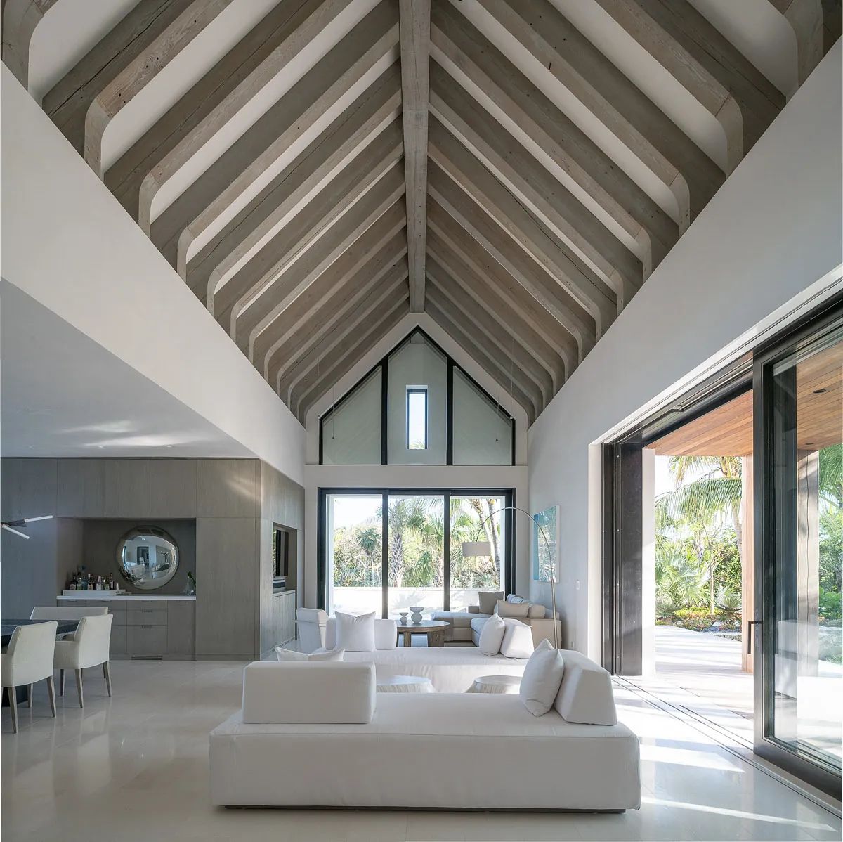 Living room with white sofa, accent chairs, coffee table, large glass doors, and exposed wooden beams.