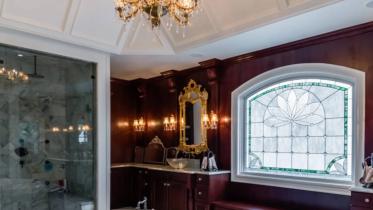 Bathroom with dark wood cabinetry, marble vanity, decorative mirror, stained glass window, and ornate ceiling details.