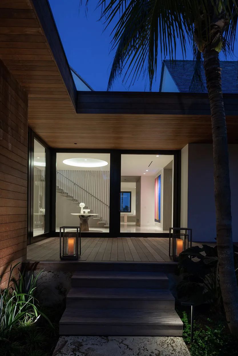 Exterior front view of a house with wooden deck, glass doors, potted plants, and lanterns.