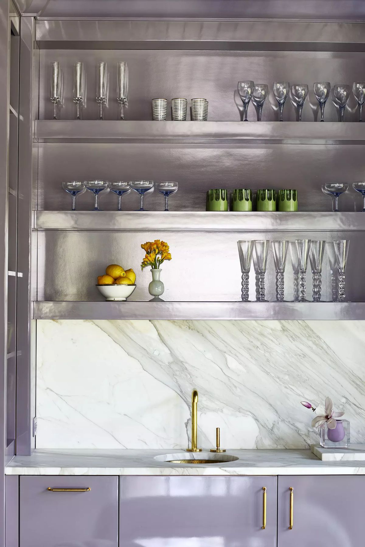 Butler's pantry with purple cabinetry, marble countertop, open shelving with glassware, and a bowl of fruit.