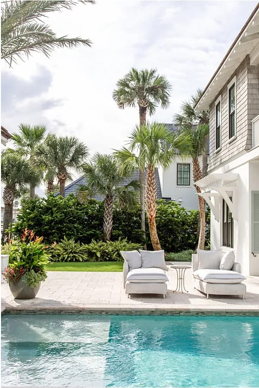 Patio with lounge chairs, side table, swimming pool, and palm trees.