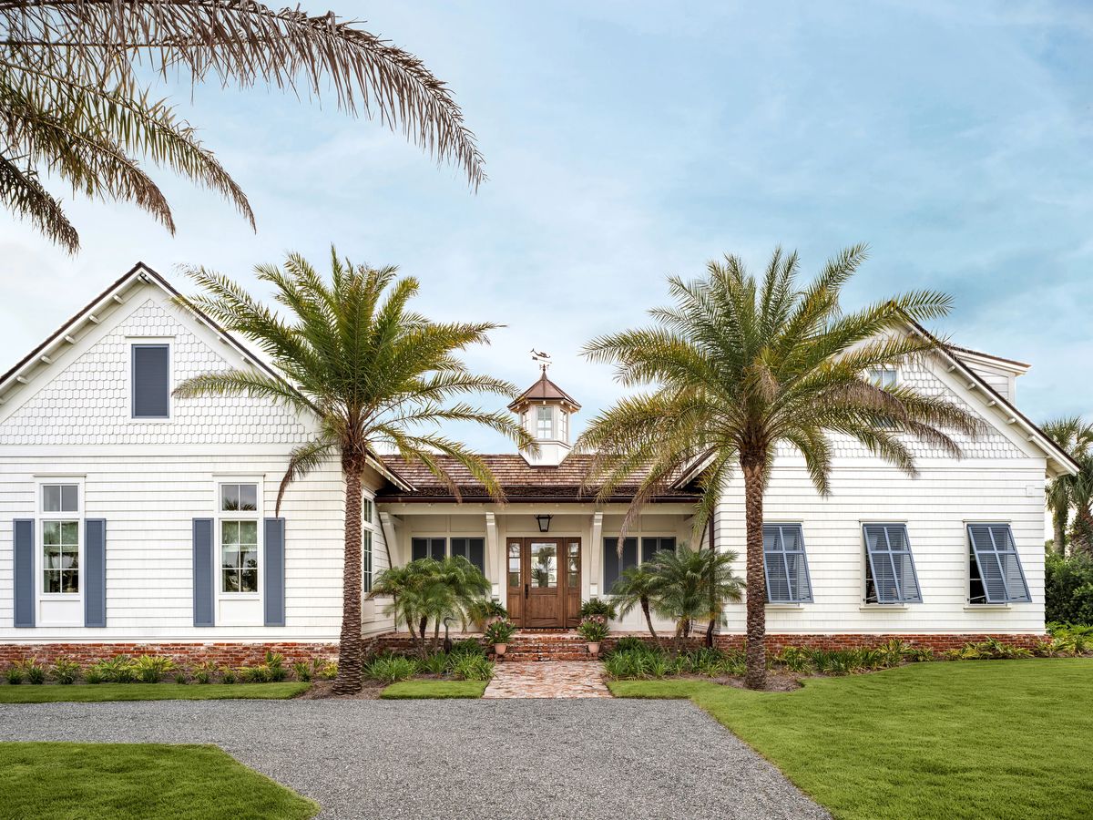 Exterior front of a house with palm trees, brick pathway, white siding, blue shutters, and a wooden door.