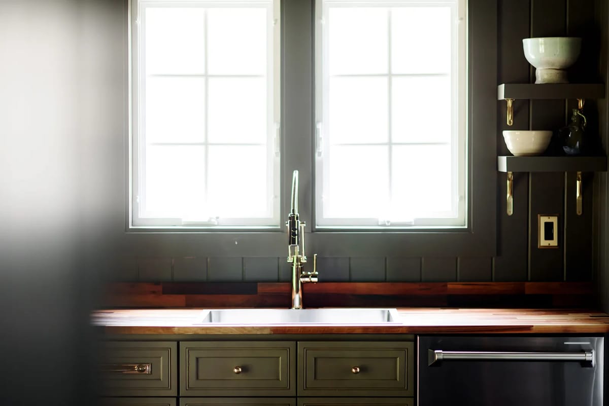 Kitchen with dark cabinetry, wooden countertop, stainless steel sink, and windows for natural light.