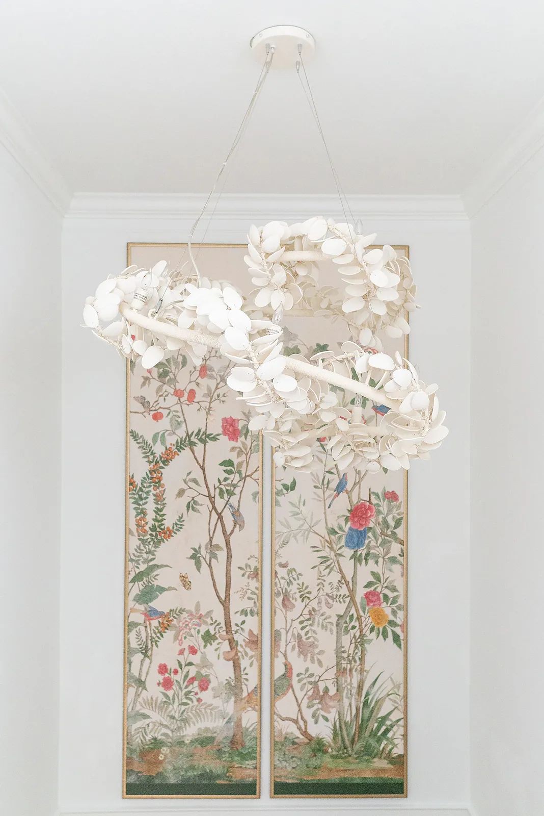 Interior space with decorative chandelier and floral artwork panels on white wall.