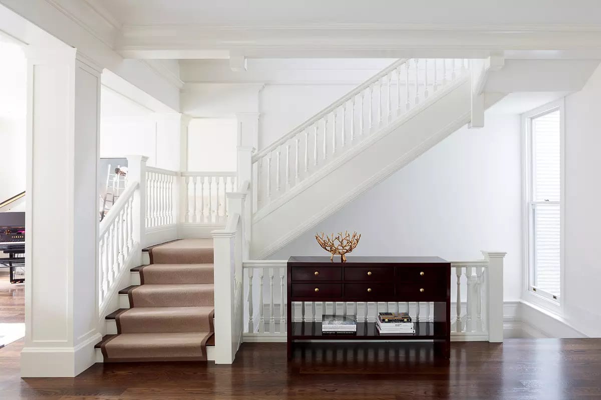 Hallway with staircase, console table, artwork, and dark wood flooring with natural light from the window