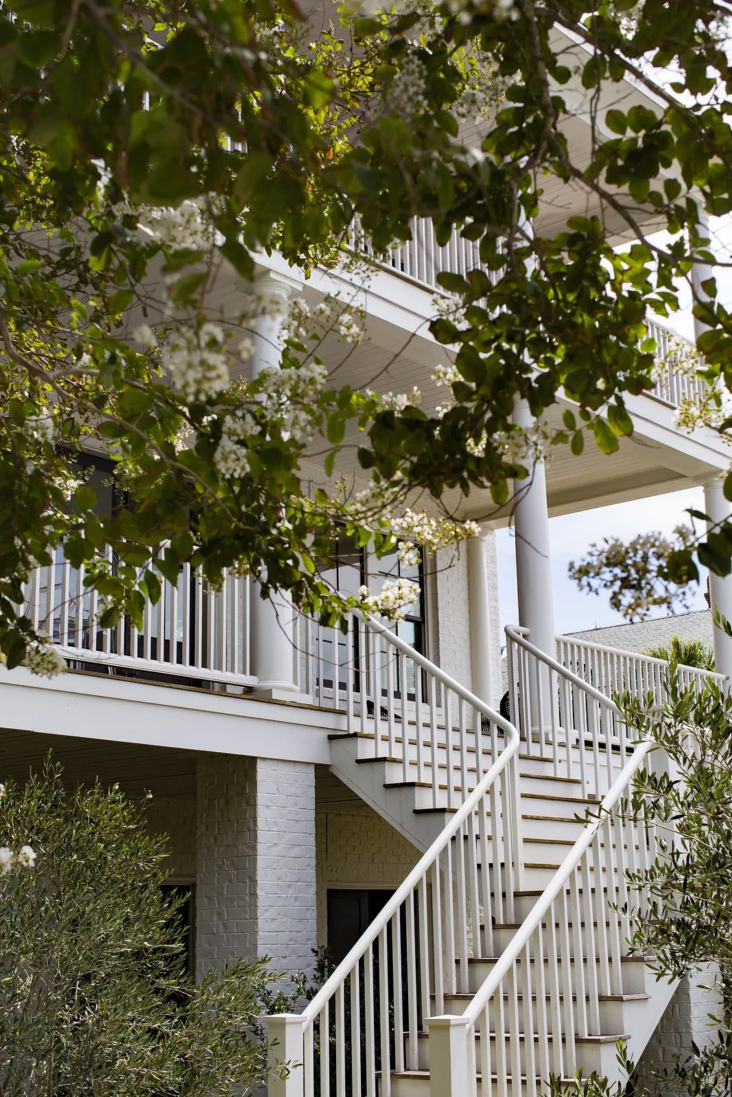 Exterior front view of a two-story building with white brick, staircase, columns, and surrounded by greenery.