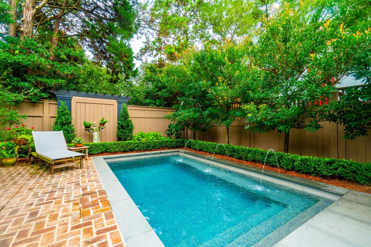 Garden area with small pool, brick paving, lounge chair, and landscaped greenery.