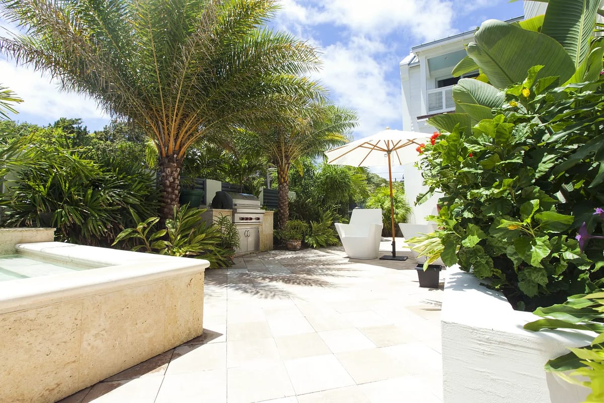 Patio with grill, outdoor chairs, umbrella, hot tub, and surrounding greenery and planters