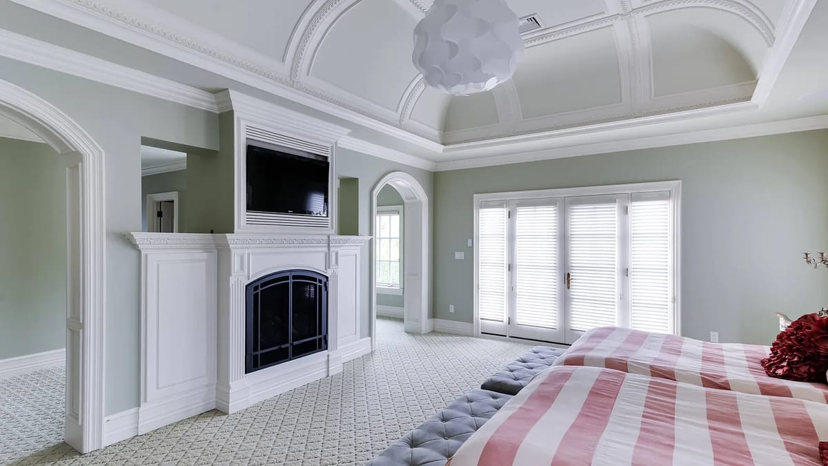Bedroom with two beds, gray ottoman, white fireplace, sliding doors, and patterned carpet.