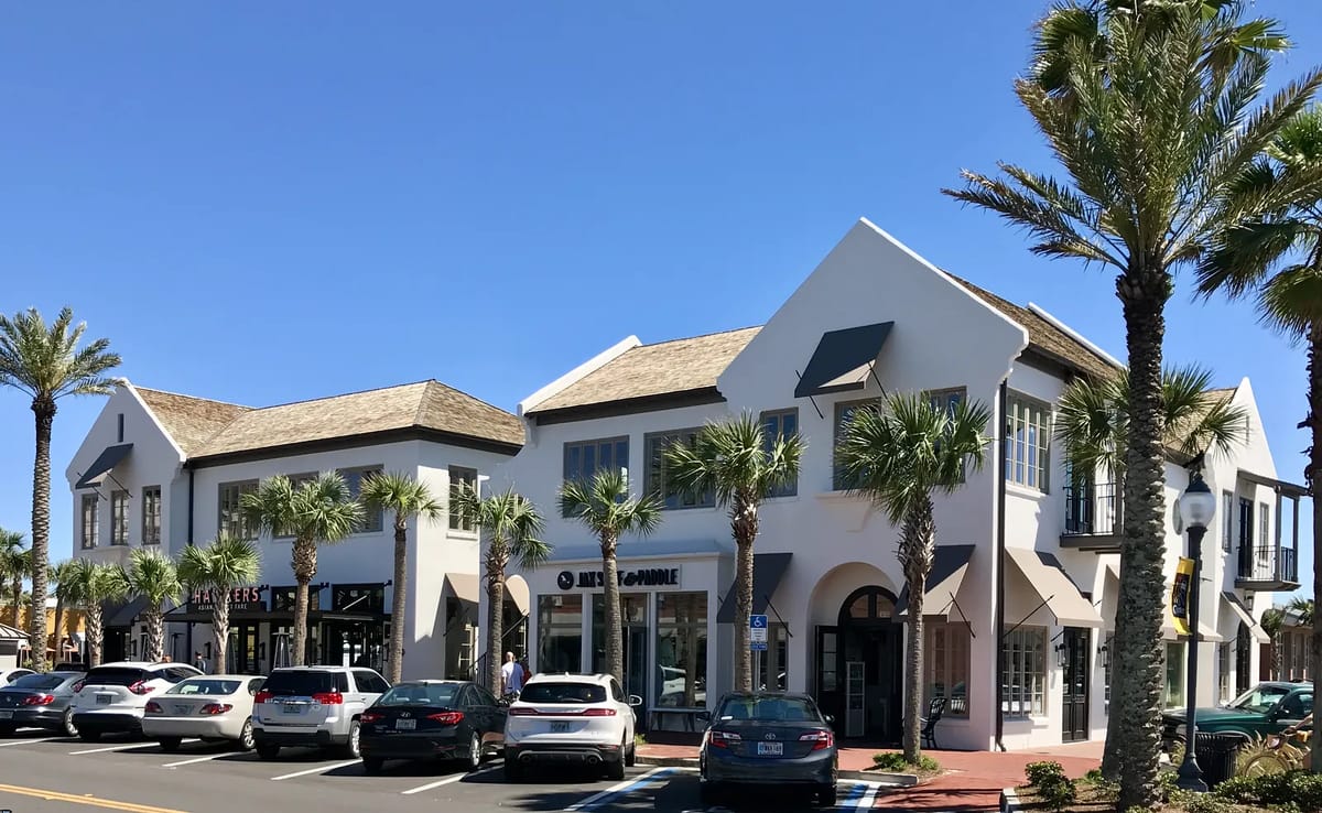 Exterior front of a two-story building with large windows, palm trees, and multiple storefronts.