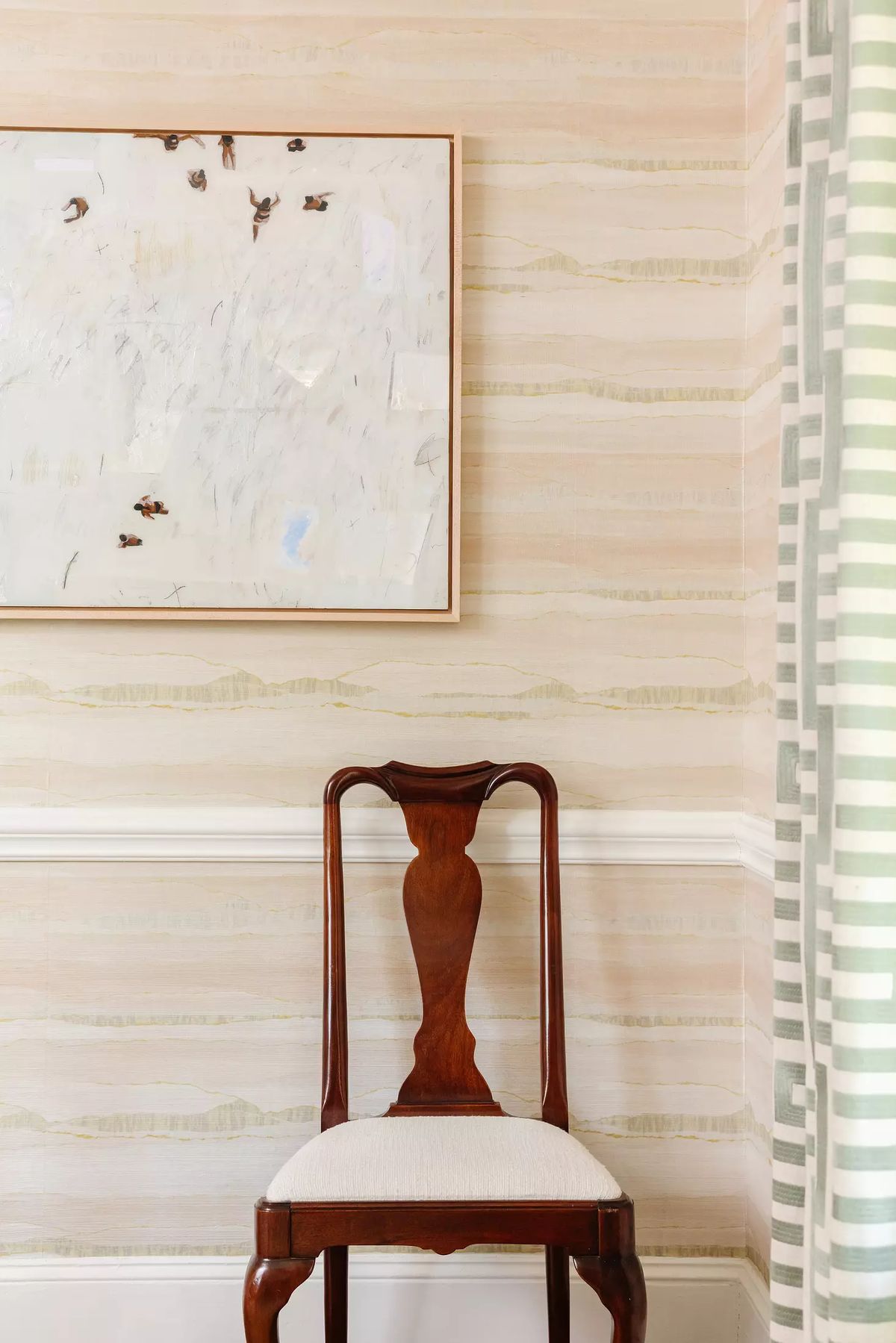 Corner with wooden chair, abstract artwork on wall, and striped curtains in a light-colored room.