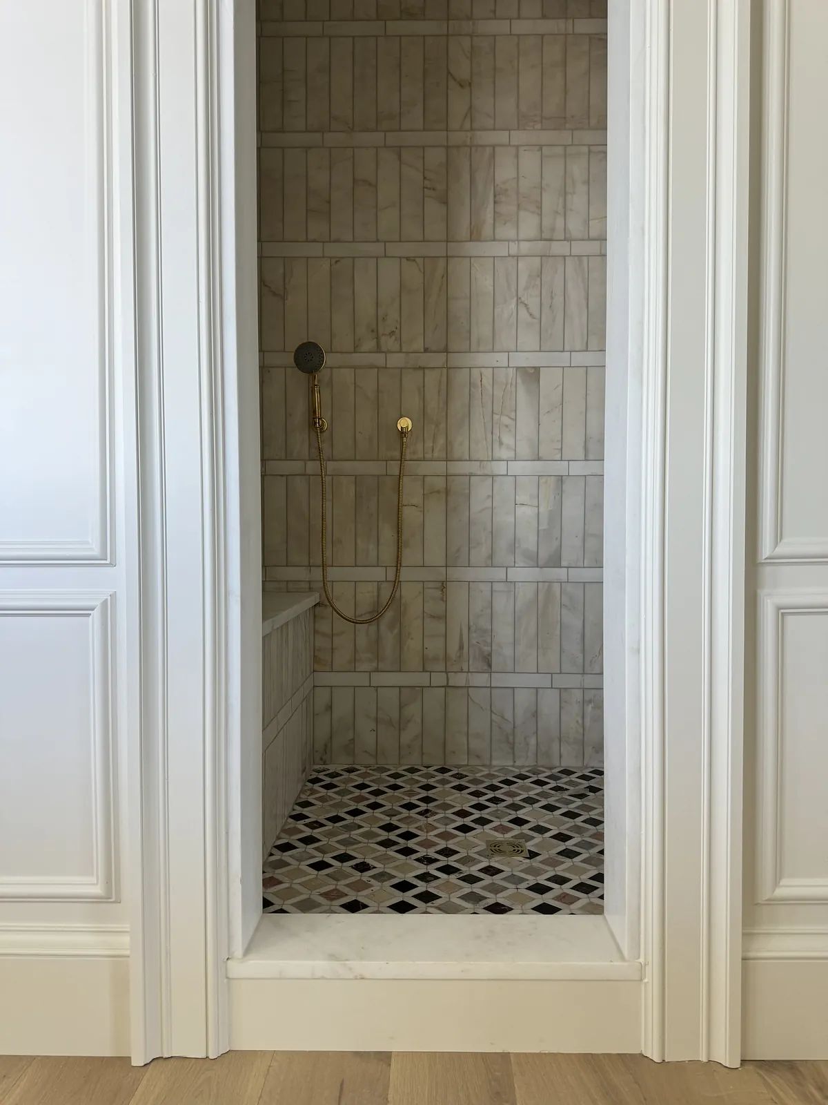 Bathroom with tiled shower area, black and white floor tiles, and gold shower fixtures.