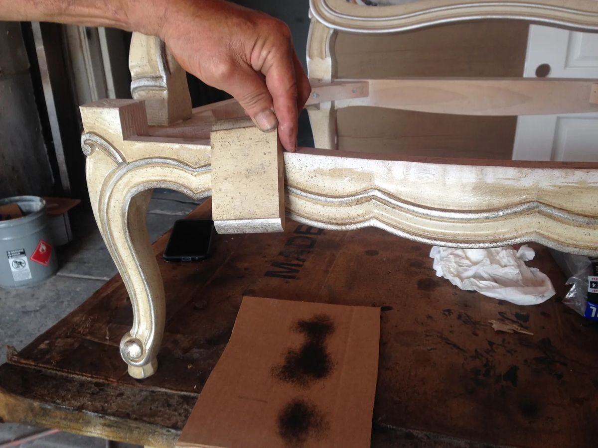 Furniture restoration showing decorative chair leg, hand, sandpaper, and cloth on wooden surface.
