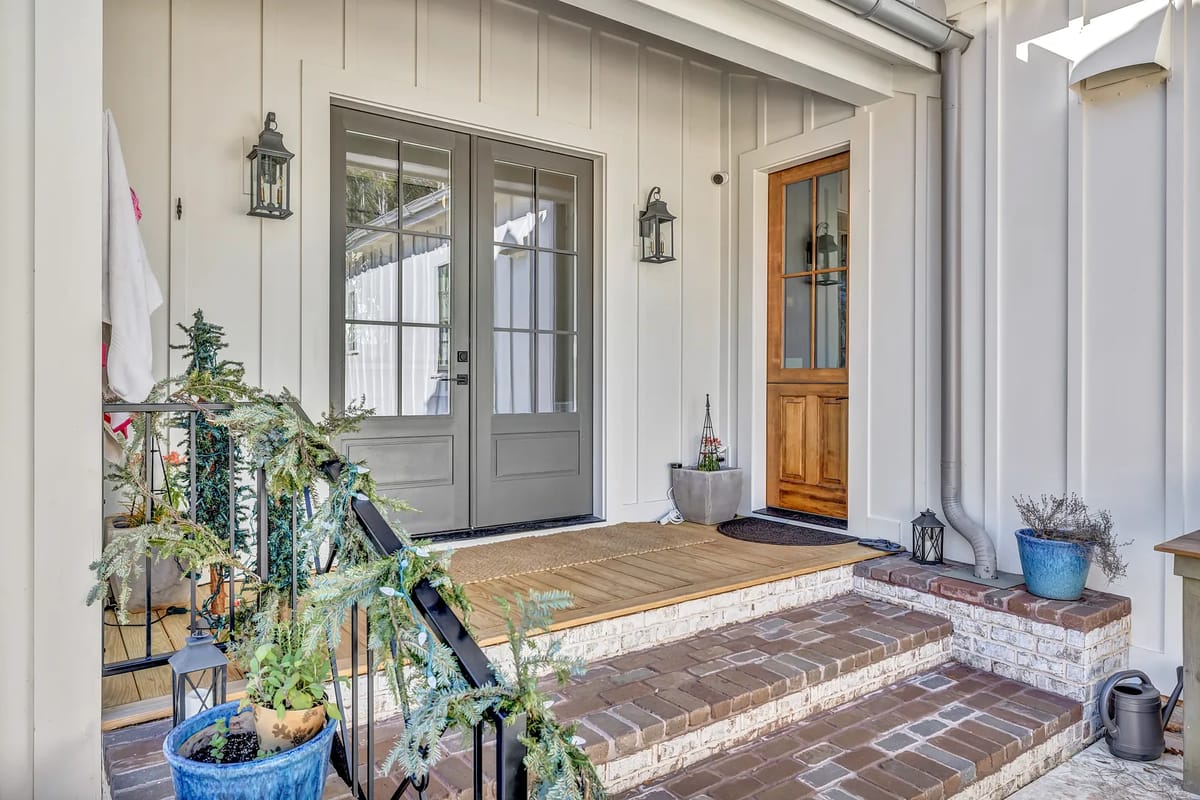Exterior front entrance with gray double doors, brick pathway, planters, and decorative accents.