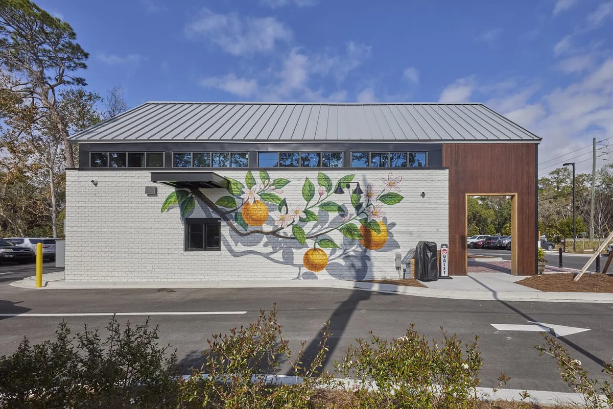 Exterior view of building with orange mural, large windows, sloped roof, and wooden paneling.