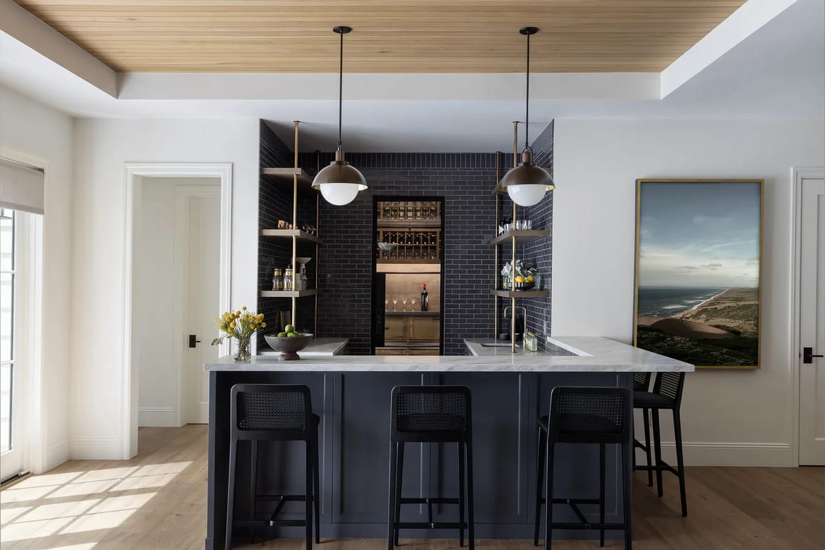 Kitchen with dark gray island, white marble countertop, black bar stools, and dark tile backsplash with wine rack