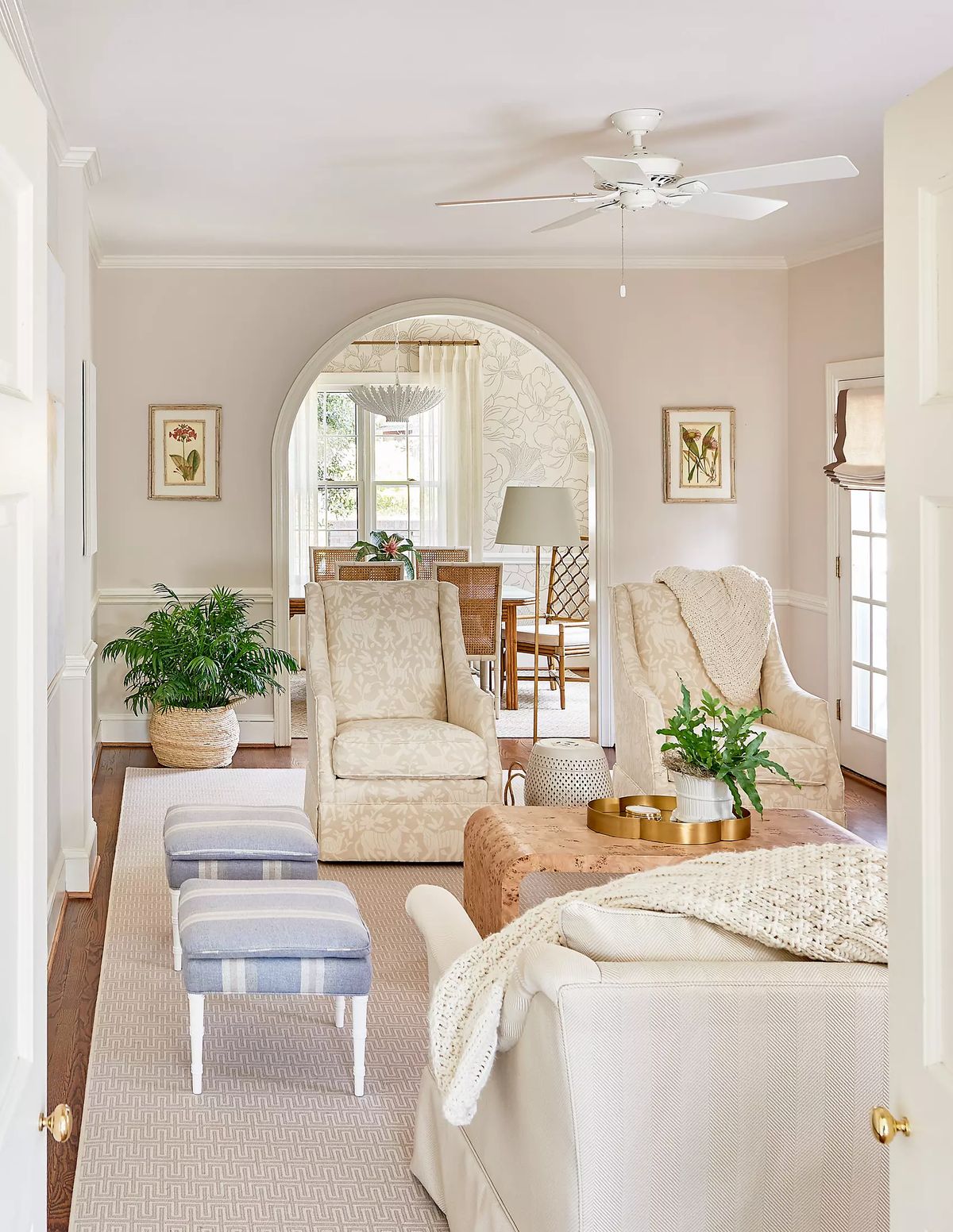 Living room with beige armchairs, light sofa, coffee table, area rug, potted plant, and archway to dining area