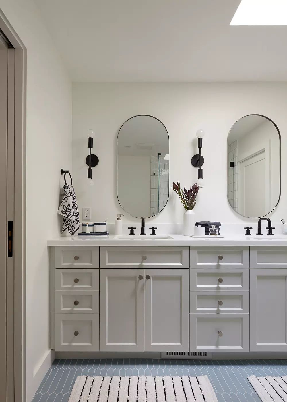Bathroom with double vanity, oval mirrors, wall sconces, and striped tile flooring.