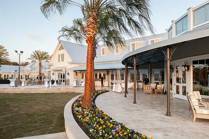Exterior area with curved stone patio, chairs, tables, flower beds, and palm trees.