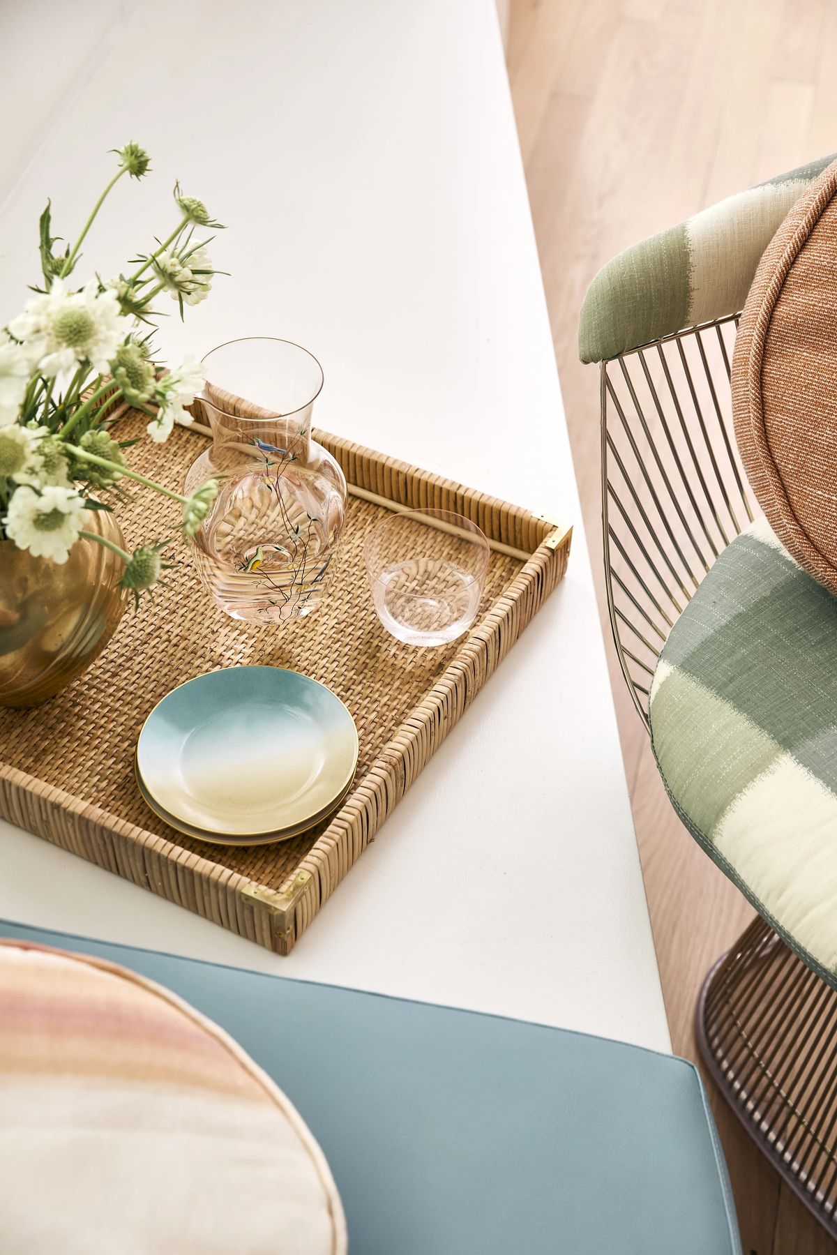 Tabletop scene with woven tray, glass vase, decorative chair, and flowers.