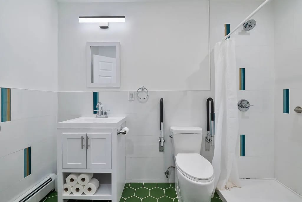 Bathroom with white vanity, toilet, shower curtain, green tile flooring, and blue-green wall accents.