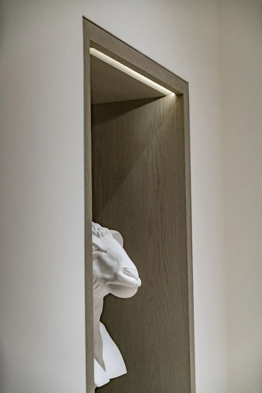 Niche with white bust sculpture on light wood shelf and recessed lighting above.