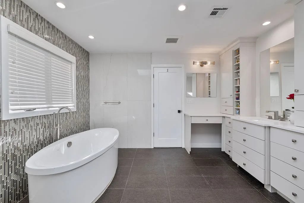 Bathroom with freestanding oval bathtub, double vanity, gray tile flooring, and a window with blinds