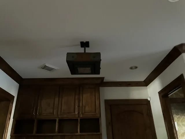 Ceiling with trim, mounted fixture, wooden cabinet, and door in a small room or alcove.