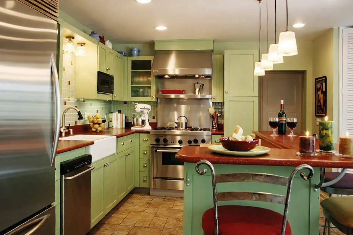 Kitchen with green cabinetry, stainless steel appliances, red countertop, bar stools, and tiled backsplash.