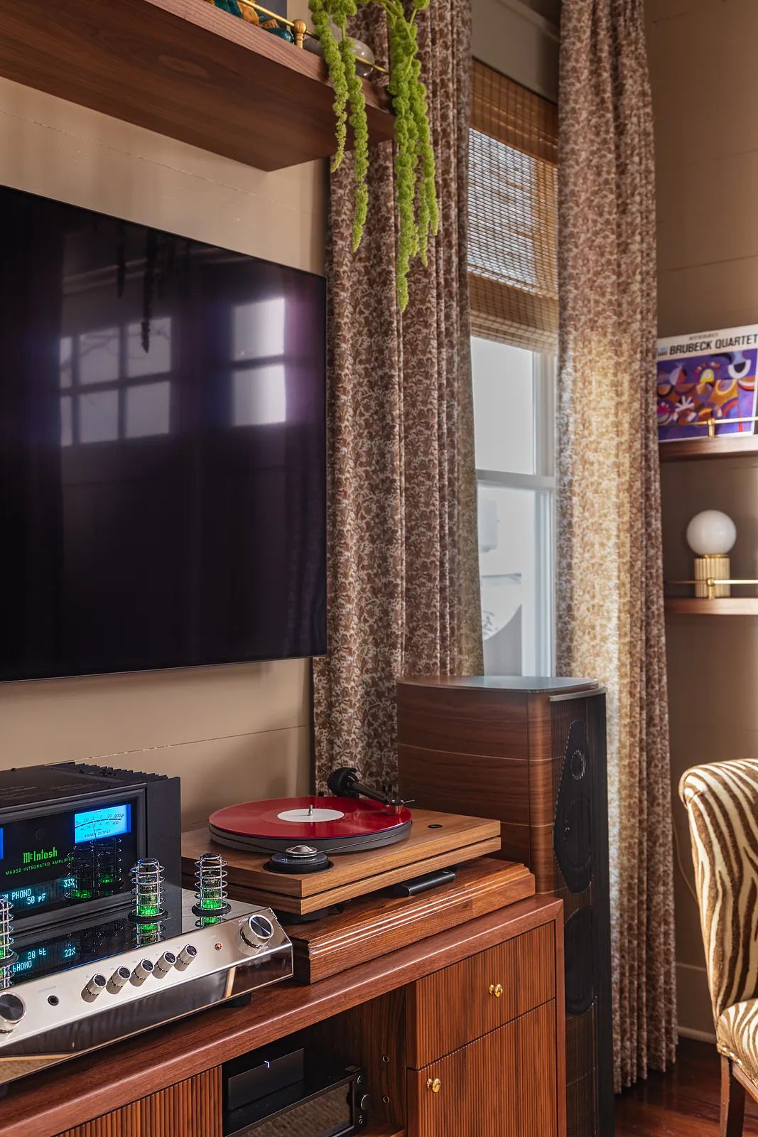 Living room with wall-mounted TV, vinyl player, wooden shelves, patterned curtains, and a striped armchair.