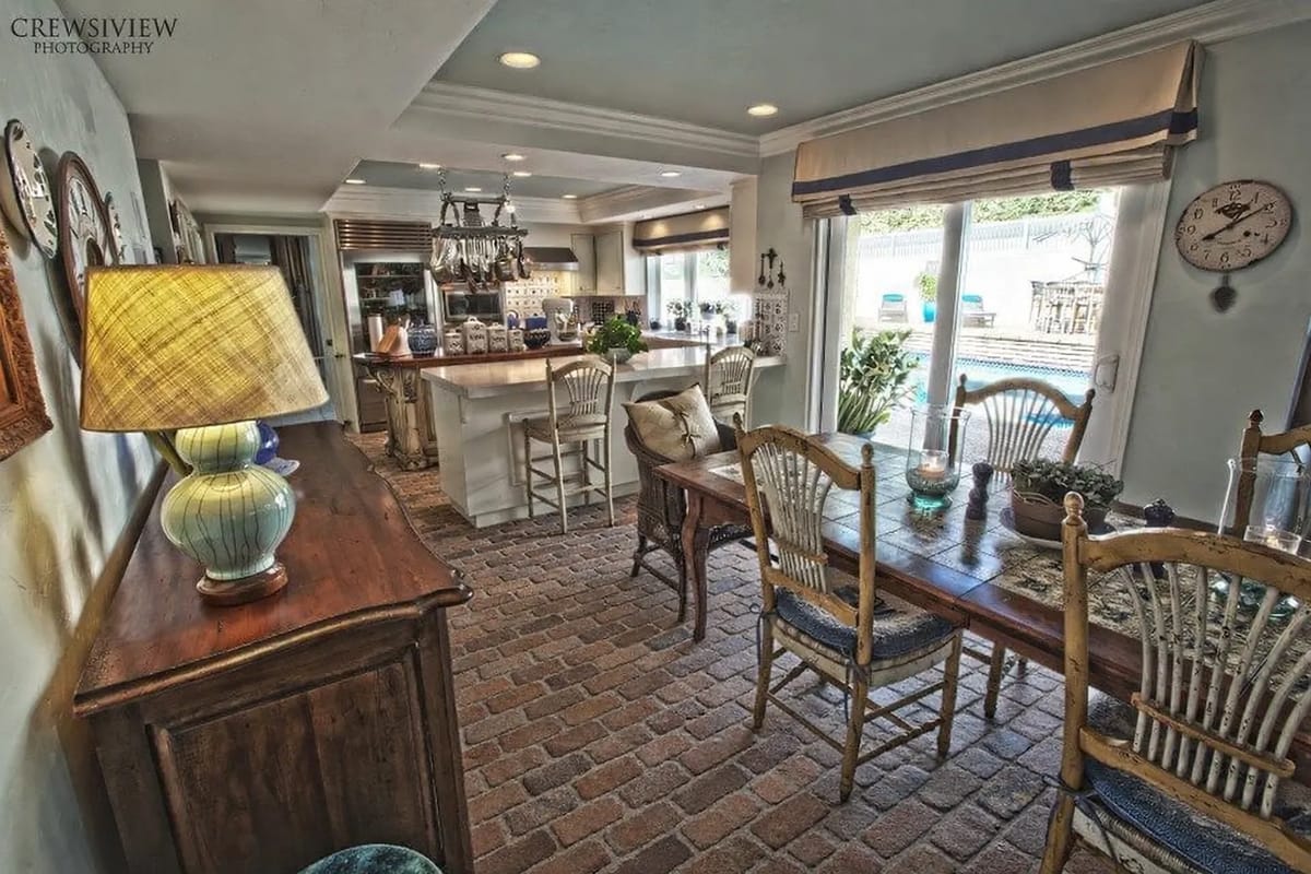 Dining room with a wooden table, six chairs, sideboard, lamp, and open kitchen area with patio views.