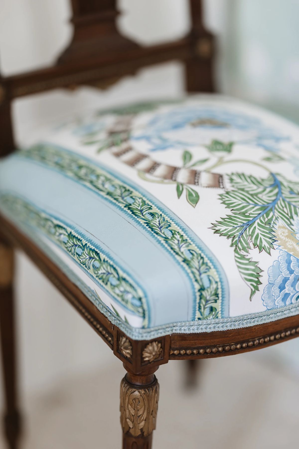 Close-up of a floral upholstered chair with carved wooden frame and detailed legs.