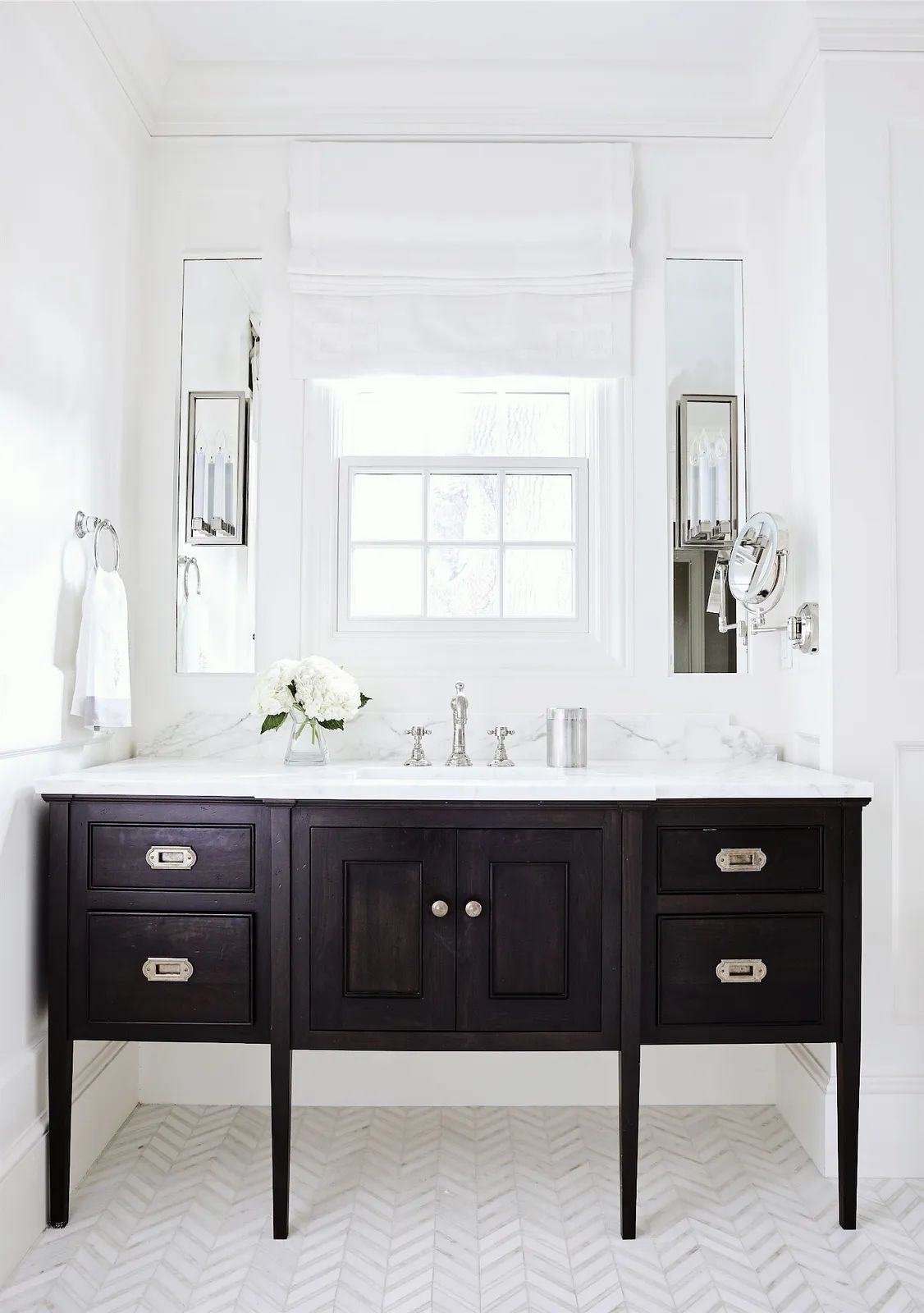 Bathroom with dark wood vanity, marble countertop, two mirrors, herringbone tile flooring, and a window.