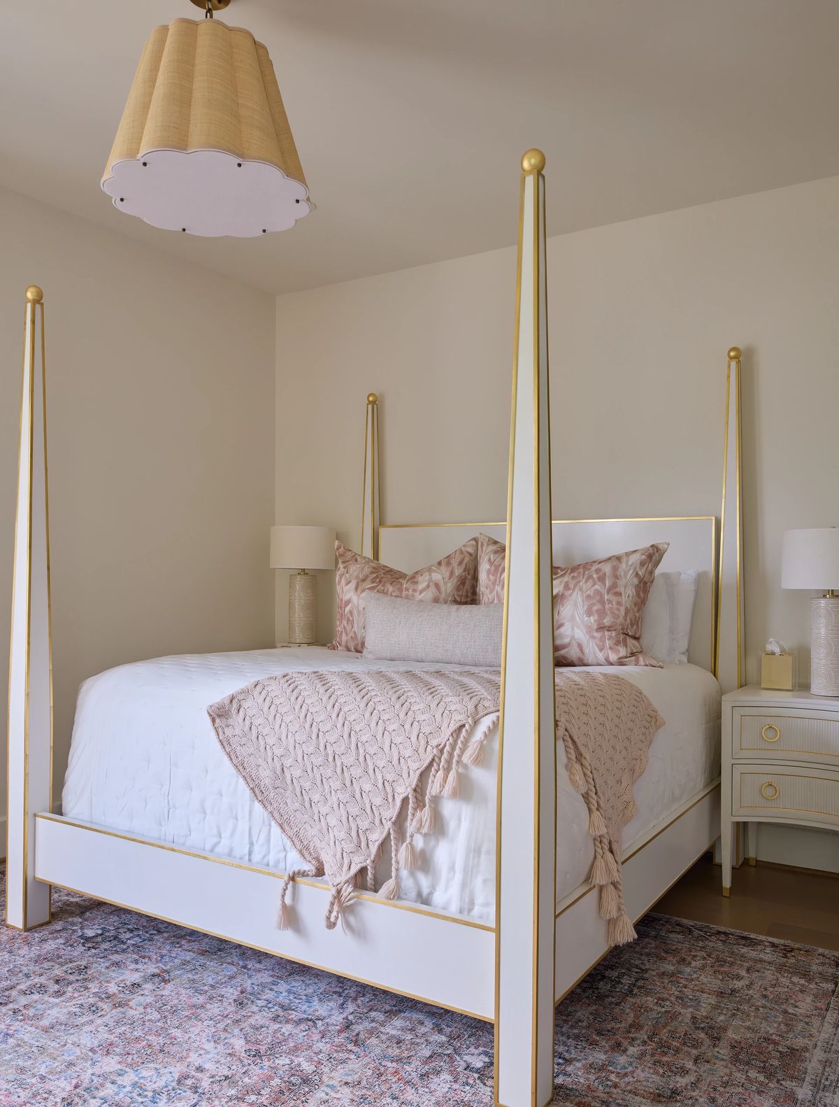 Bedroom with four-poster bed, white quilt, pink pillows, nightstand, lamp, and area rug.