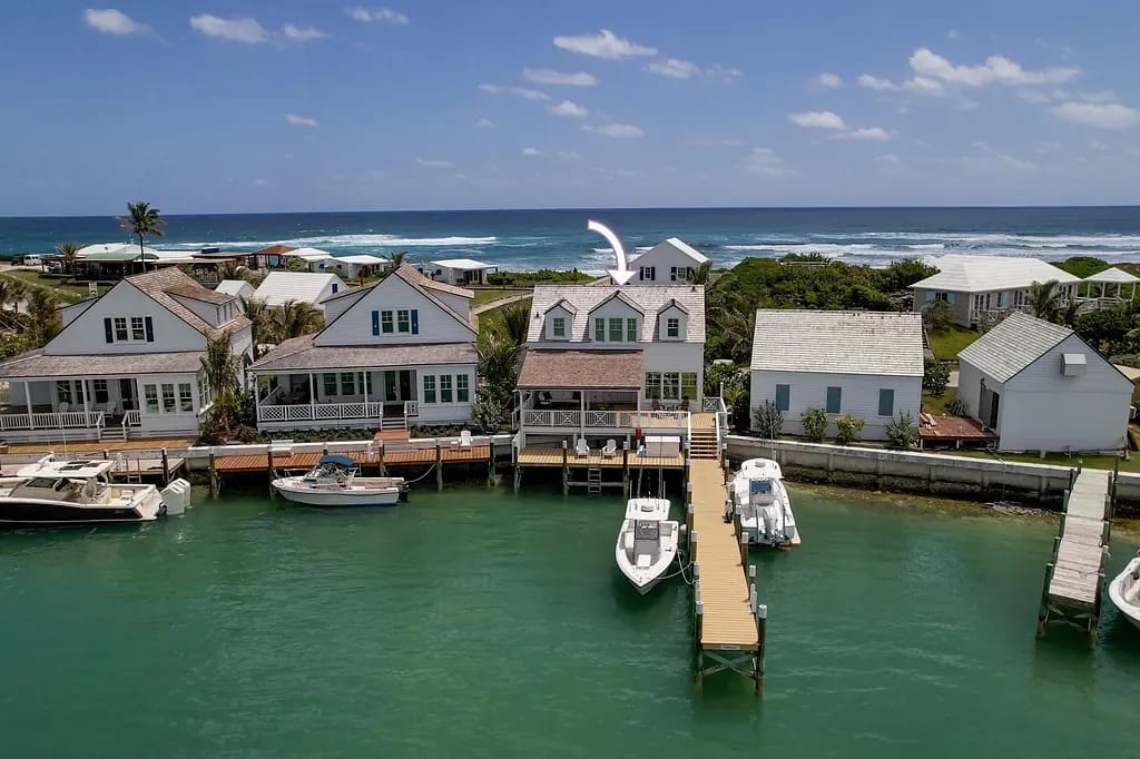 Waterfront view of houses along a canal with boats, pier, and ocean in the background.