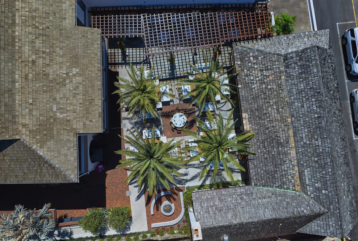 Patio with dining tables, chairs, palm trees, circular stone path, and ornamental plants.