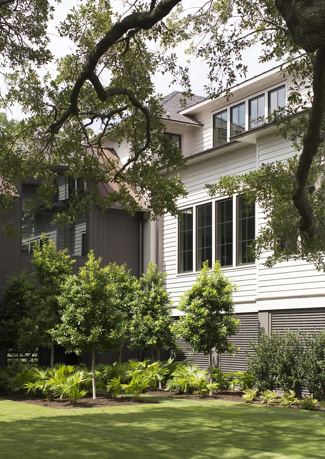Exterior rear view with two buildings, white and dark siding, trees, shrubs, and grassy area.