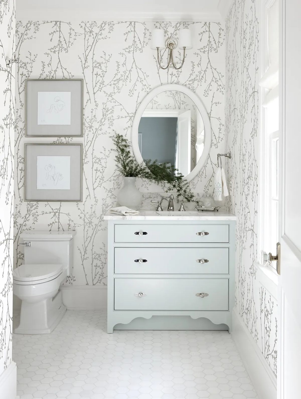 Bathroom with light blue vanity, round mirror, decorative wall art, and white floral-patterned wallpaper