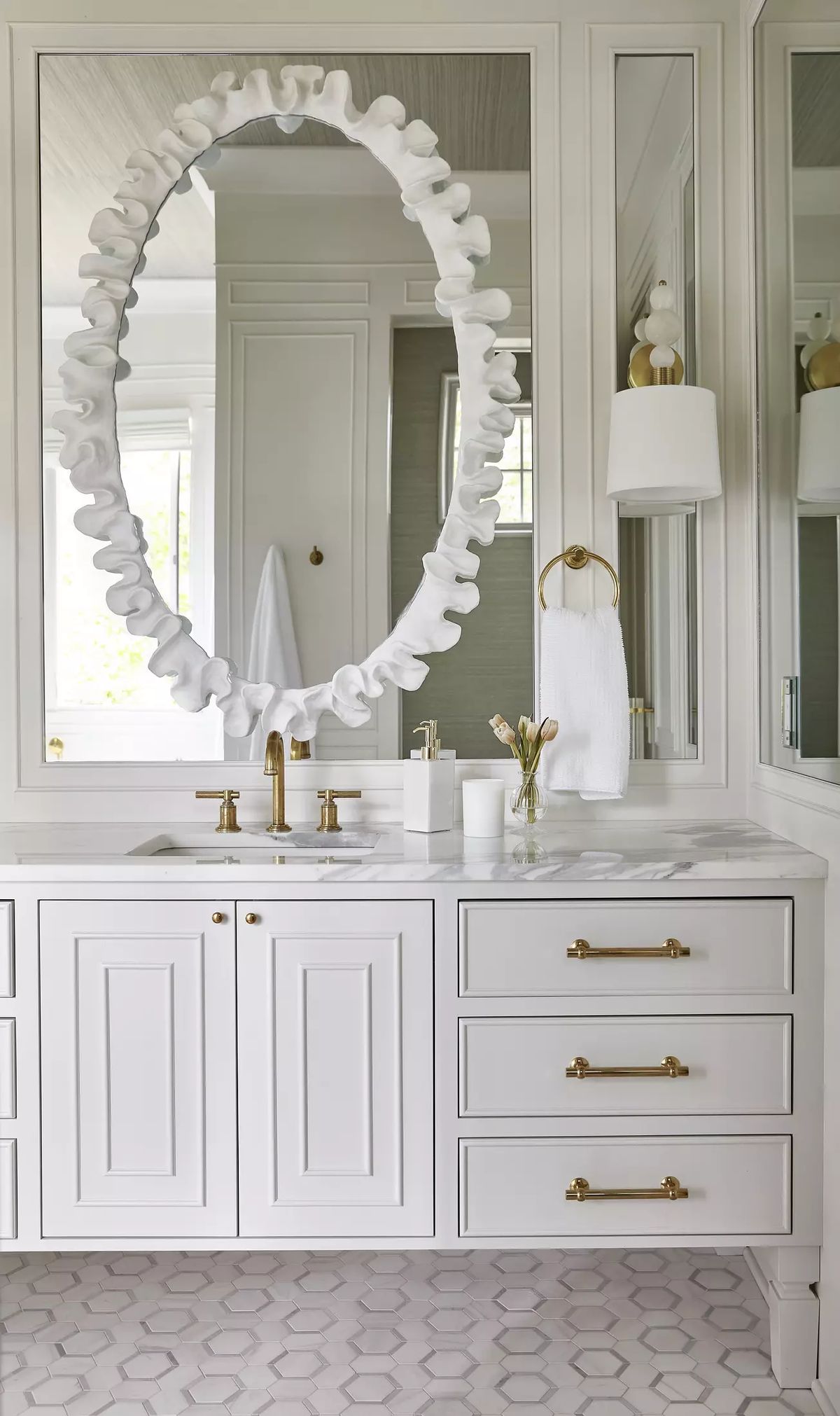 Bathroom with white vanity, gold hardware, ruffled mirror, wall sconce, and hexagonal tile flooring