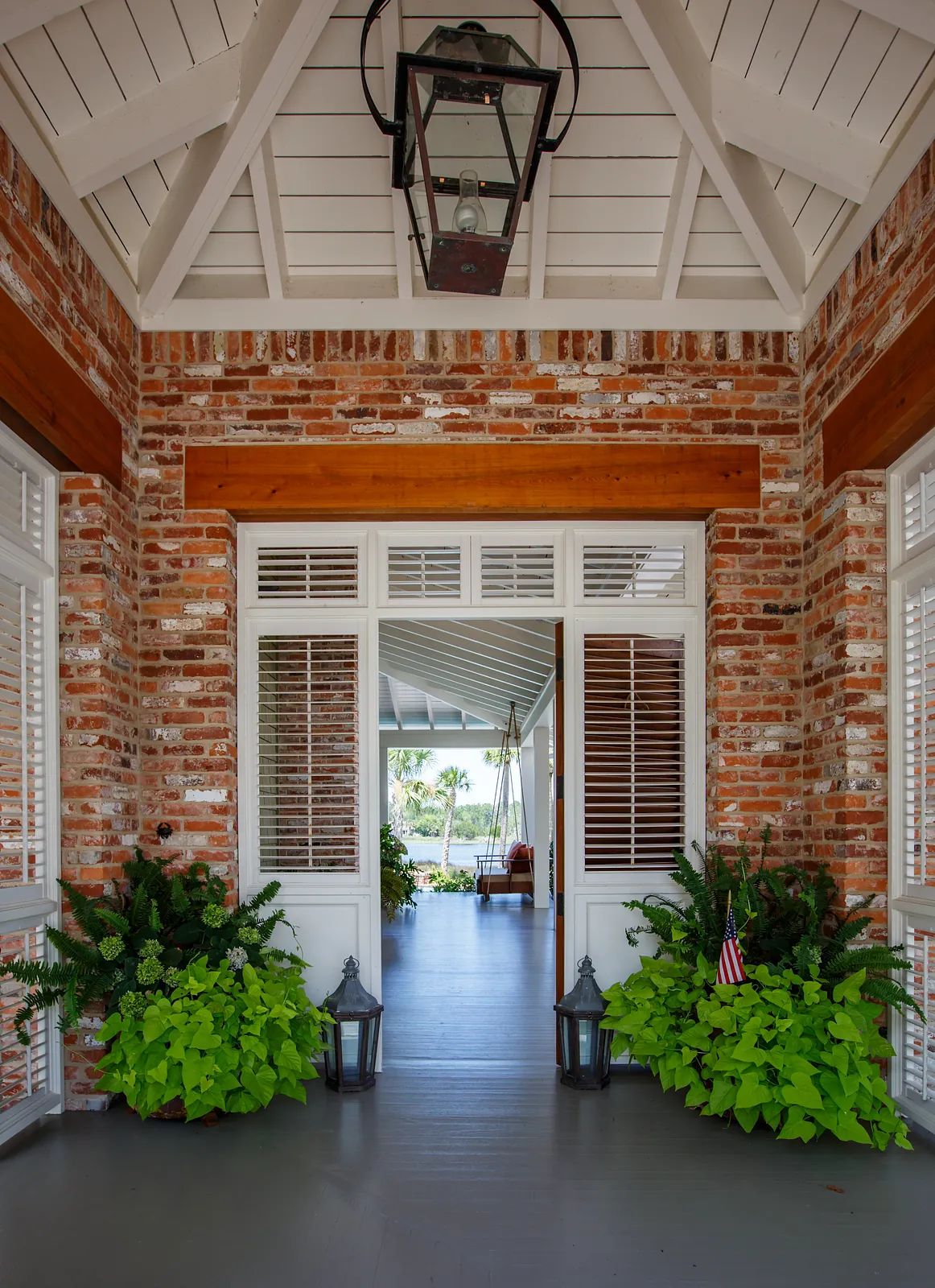 Foyer with rustic brick wall, white double doors, greenery, wooden beams, and lantern fixture