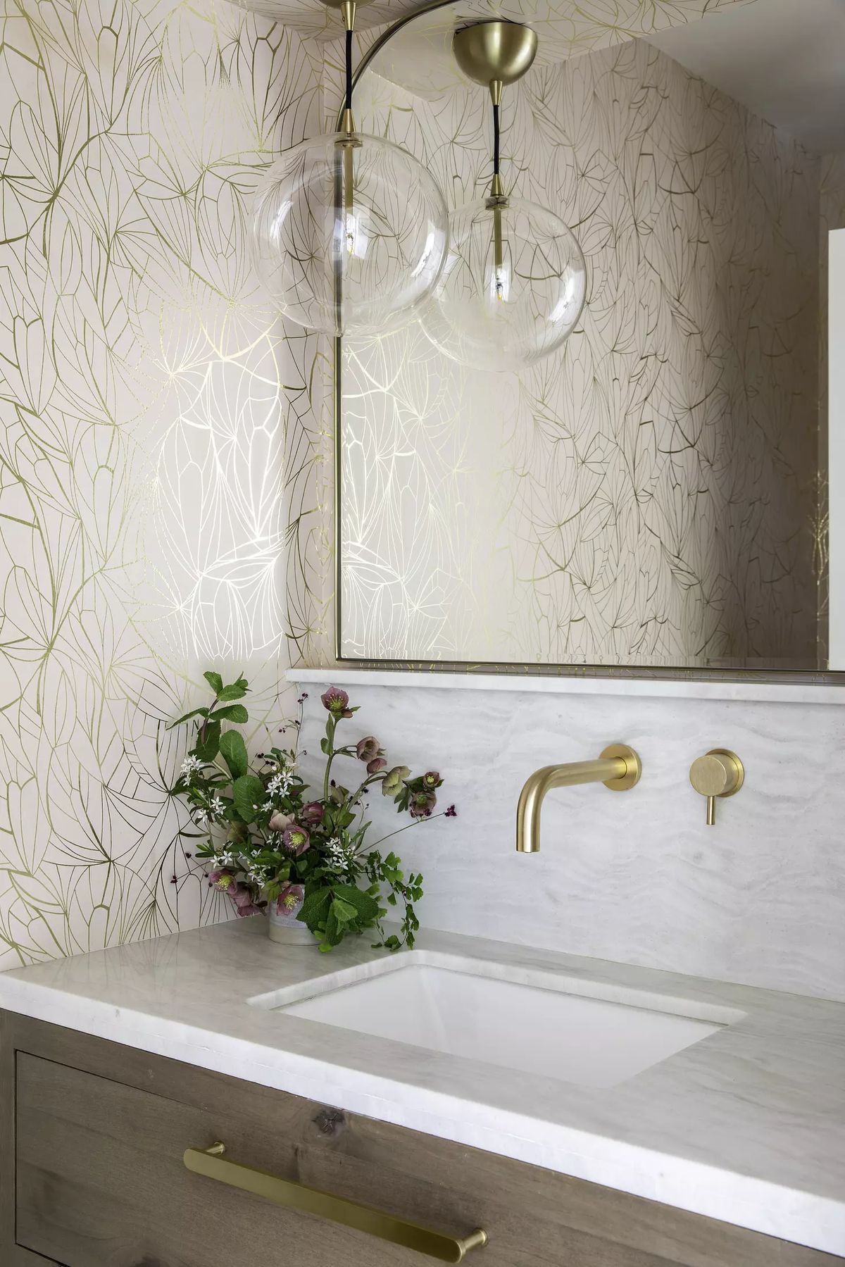 Bathroom with marble countertop, under-mount sink, gold fixtures, and pink wallpaper with gold leaf patterns.