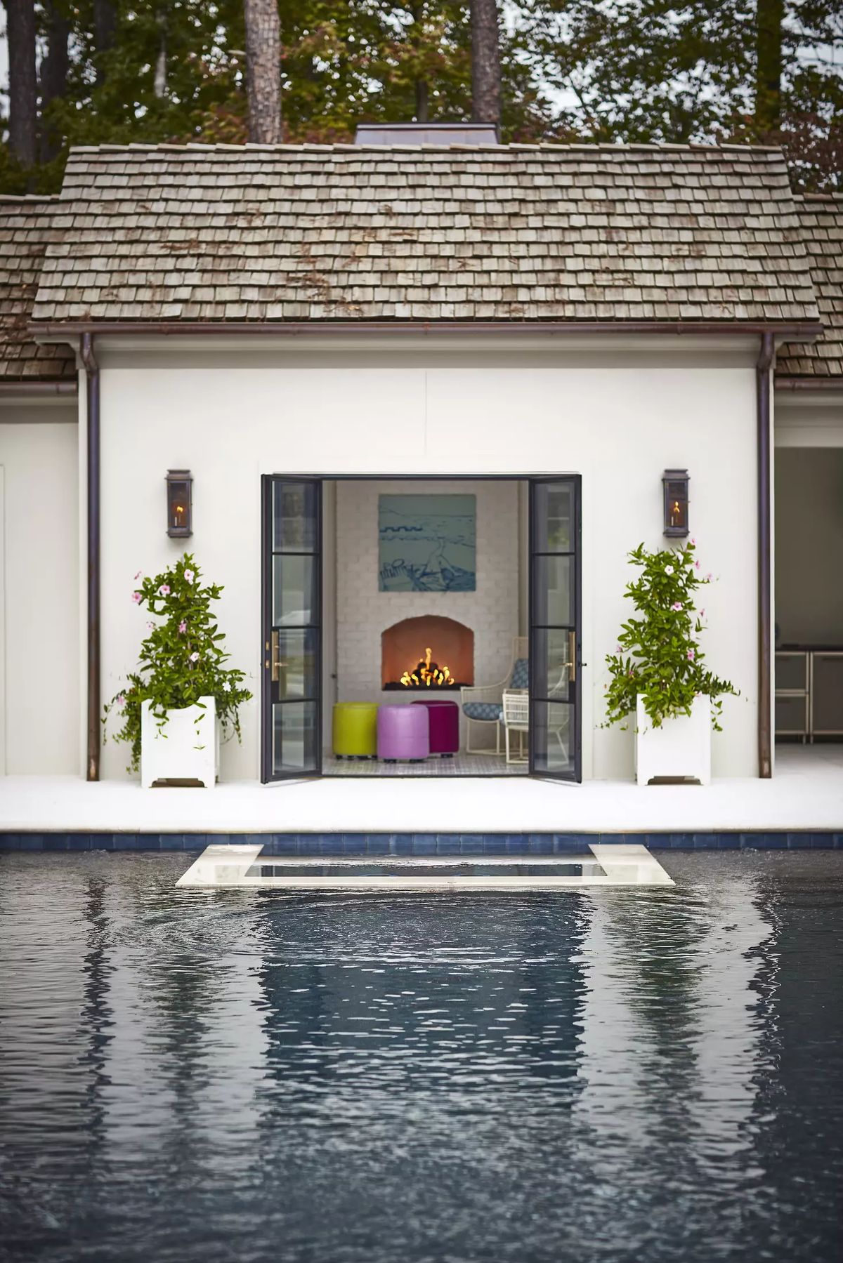 Exterior space with swimming pool, double doors, seating area with fireplace, and flower pots.